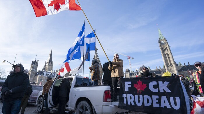 Un manifestante ondea una bandera canadiense volcada frente al Parlamento de Ottawa; otro sostiene una pancarta en la que se lee un grosero insulto contra el primer ministro Justin Trudeau.