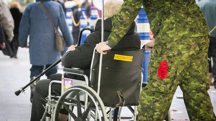 Un militaire des Forces armées canadiennes pousse une personne dans un fauteuil roulant.