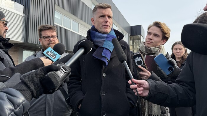Bruno Marchand est entouré de journalistes qui tendent des micros.