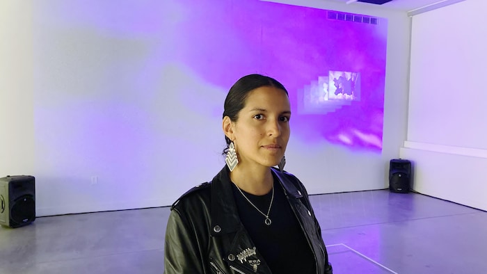Woman (interdisciplinary artist Laura Criollo Carrillo) looks into the camera.  Derrière elle, son oeuvre Ville superposées. 