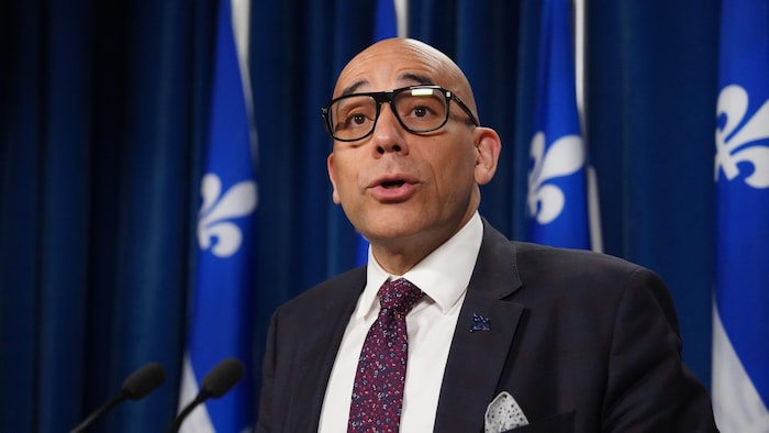 Devant des drapeaux du Québec, Christopher Skeete parle lors d'une conférence de presse.