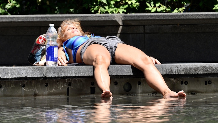 Une femme essaie de se rafraîchir à Montréal en pleine canicule avec les pieds dans une fontaine et une grande bouteille d'eau.