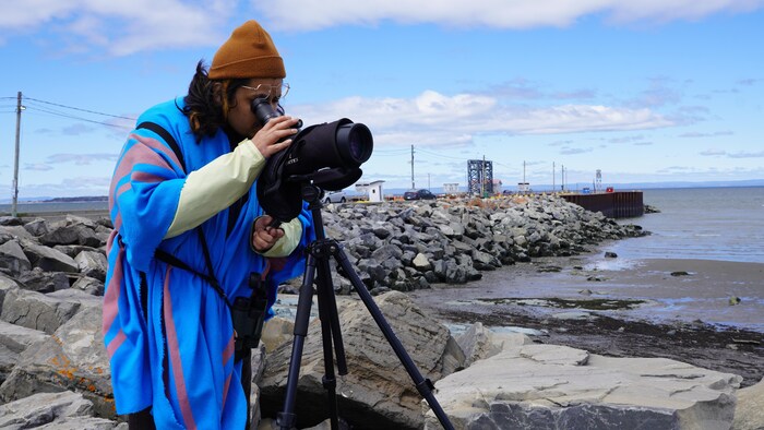 Ivar Alberto Delgado Sifuentes observe à l'aide d'une lunette d'approche des oiseaux marins au quai de Trois-Pistoles.