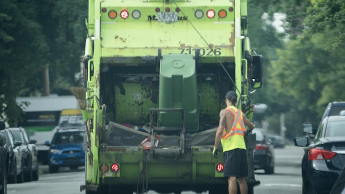 Un éboueur derrière un camion à ordures.