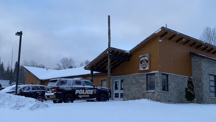 Un bâtiment avec des autos de police devant sous la neige.