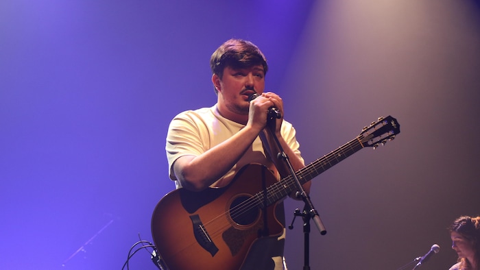 Un homme avec une guitare chantant au micro. 