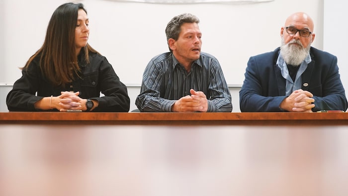 Johannie Blais, Michel Dubé et Roger Harvey sont assis devant une table en bois lors de la conférence de presse. 