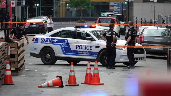 Des policiers près d'une voiture de patrouille derrière des rubans et des cônes orange.