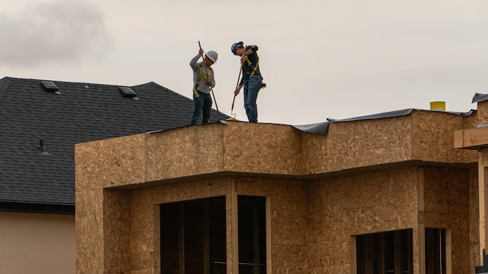 Deux personnes avec des harnais travaillent sur une maison en construction.