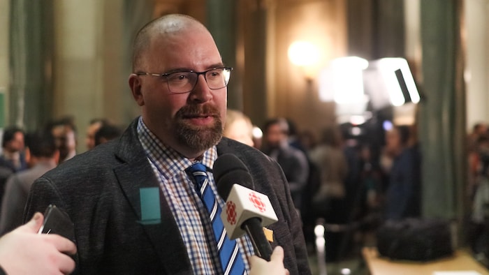 Denis Simard face aux journalistes, un micro de Radio Canada devant lui.