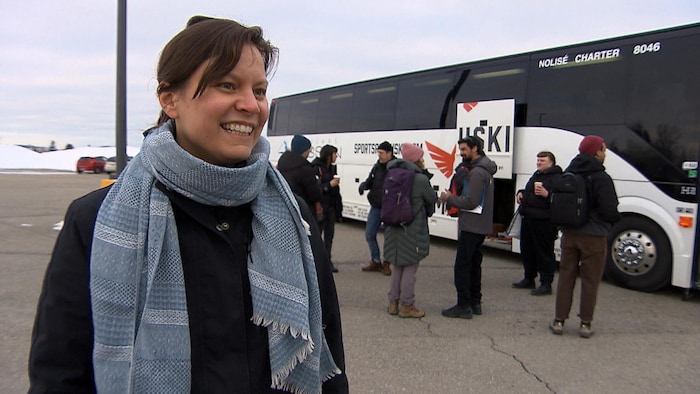 Portrait d'Émilie Pelletier, porte-parole régionale du mouvement « Le communautaire à boutte », devant un autocar et des manifestants qui s'apprêtent à partir pour Québec.