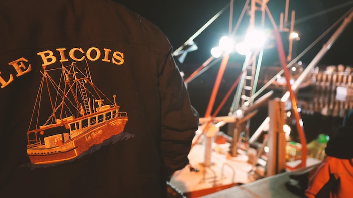 Un pêcheur portant un manteau inscrit «Le Bicois» regarde son bateau de pêche.