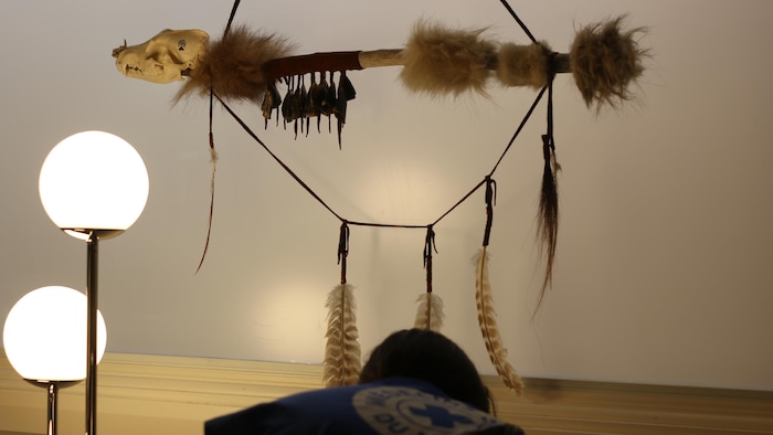 Une personne sous une oeuvre faite d'ossements, de plumes et de fourrure. 