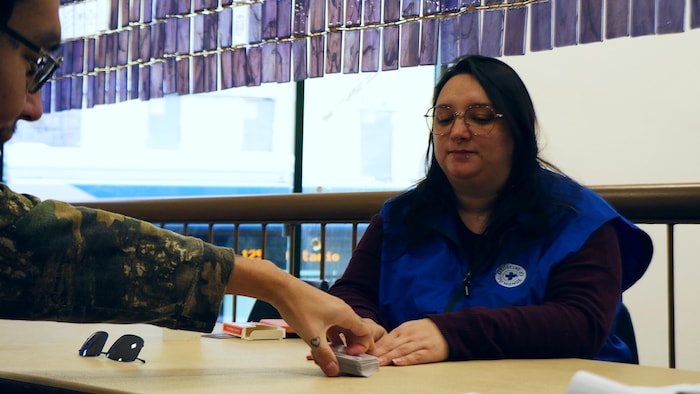Une femme et un homme jouent aux cartes sous un grand wampum accroché près d'eux. 