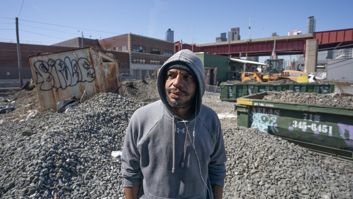 Adam Catrini au milieu d'un terrain rempli de gravats et de conteneurs.