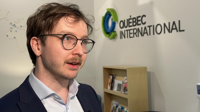 Un homme avec une moustache et des lunettes en entrevue dans un bureau.