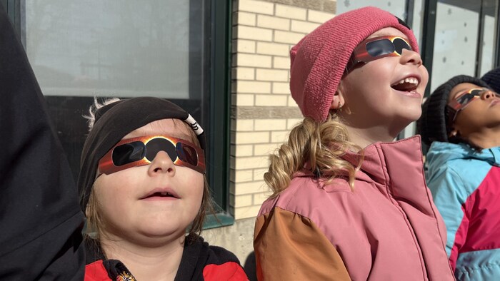 Des enfants regardent le ciel avec des lunettes de protection. 