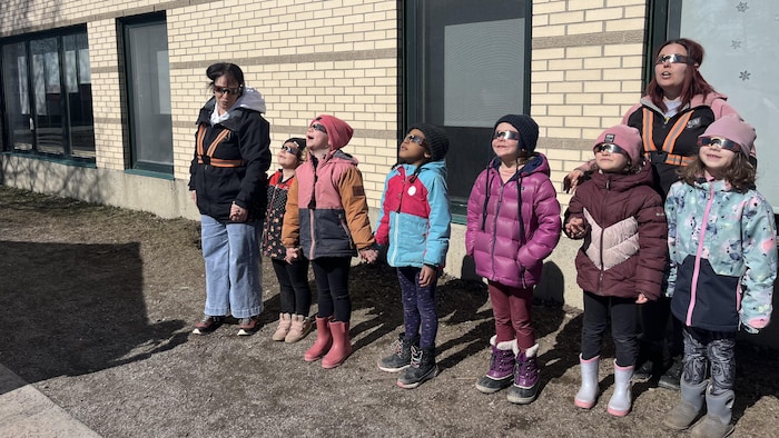 Six enfants et deux adultes regardent le ciel avec des lunettes de protection. 