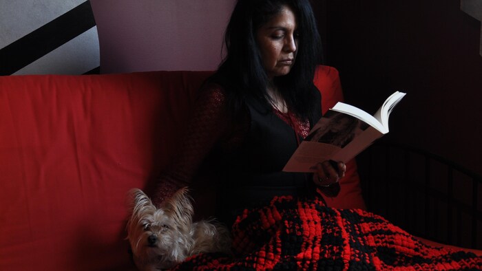 Une femme (l'écrivaine canado-péruvienne Roxana Orué) lit un livre sur un sofa. Un petit chien est à ses côtés. 
