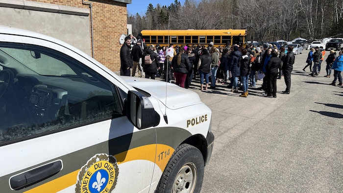 Des élèves sont rassemblés à l'extérieur entre un autobus scolaire et un véhicule de la Sûreté du Québec.