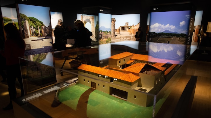 Représentation en miniature d'une maison de Pompéi entourée de photos de vestiges de la ville.