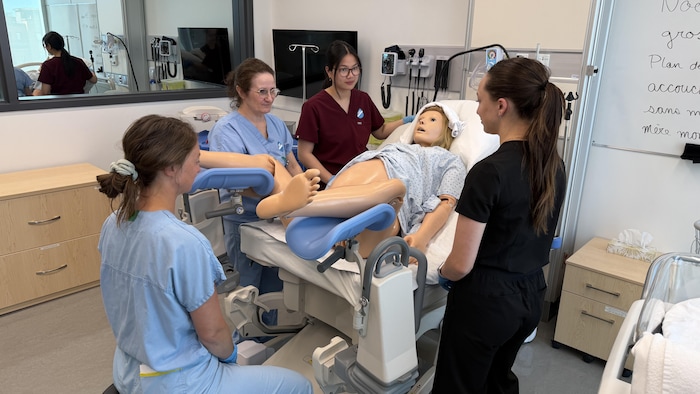 Des étudiants et professionnels de la santé autour d'un mannequin représentant une femme enceinte.
