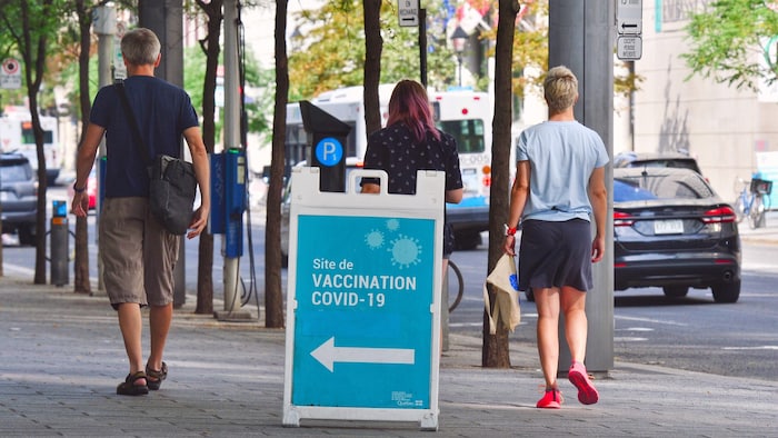 Des passant marchent sur la rue devant l'affiche d'un centre de vaccination. 