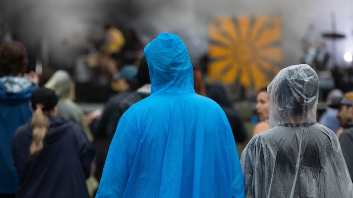Des festivaliers vêtus de ponchos se protègent de la pluie.
