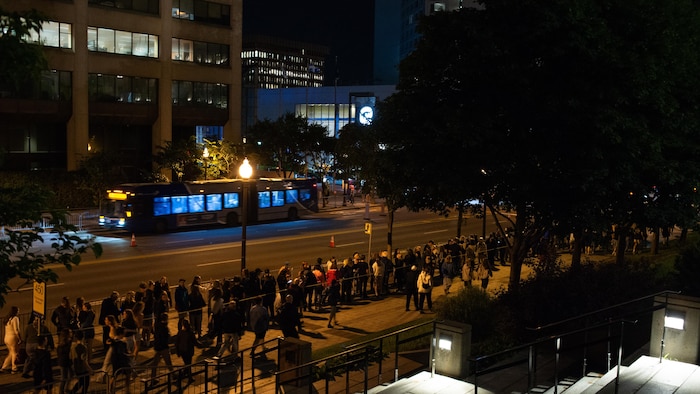 Un autobus au loin et une file de monde qui attend.