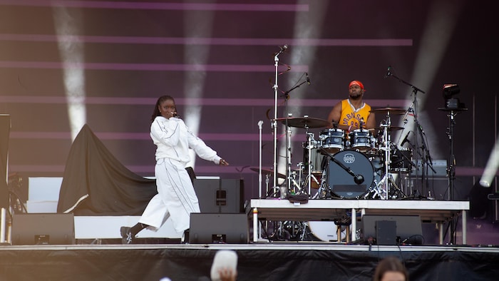 La rappeuse marche en chantant sur la scène devant le batteur.