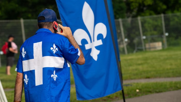 A man dressed in a t-shirt with the Quebec flag walks by talking on the phone. national day show quebec: public