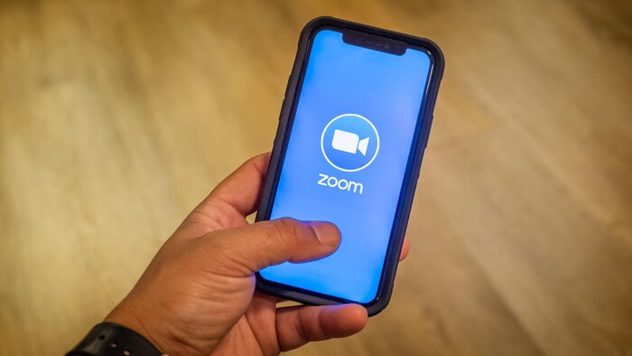 Une main tenant un téléphone avec l’application Zoom à l'écran.