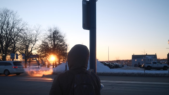 Une personne attend l'autobus alors que le soleil se lève au-dessus de la rivière Petitcodiac.