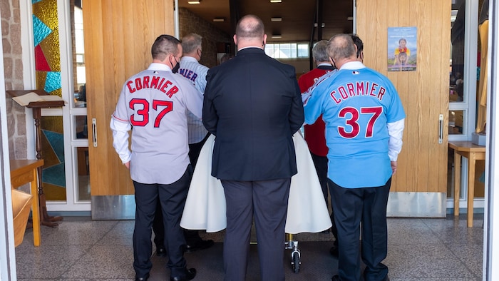 Les porteurs photographiés de dos alors qu'ils entrent dans l'église avec le cercueil. Ils portent des chemises de baseball des équipes pour lesquelles Rhéal Cormier a joué.
