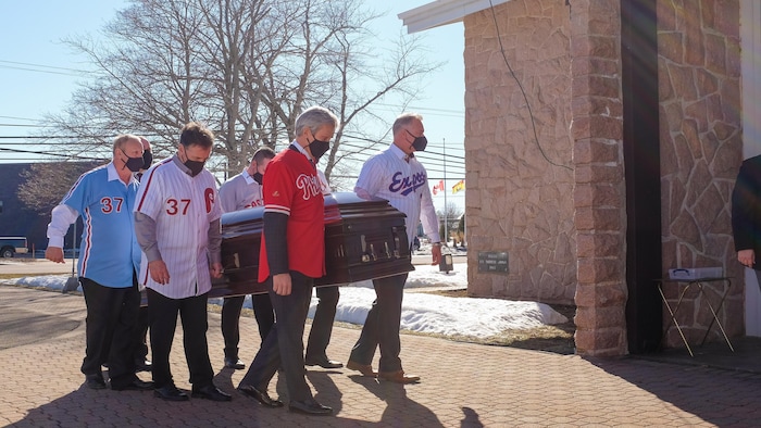 Les porteurs vêtus de chemises de baseball s'apprêtent à entrer dans l'église avec le cercueil.
