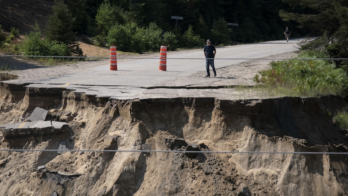 Un homme marche vers le bord d'une grosse crevasse au beau milieu d'une route.