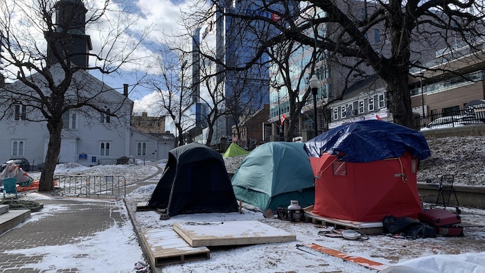 Quelques tentes sur une place publique avec un peu de neige au sol.