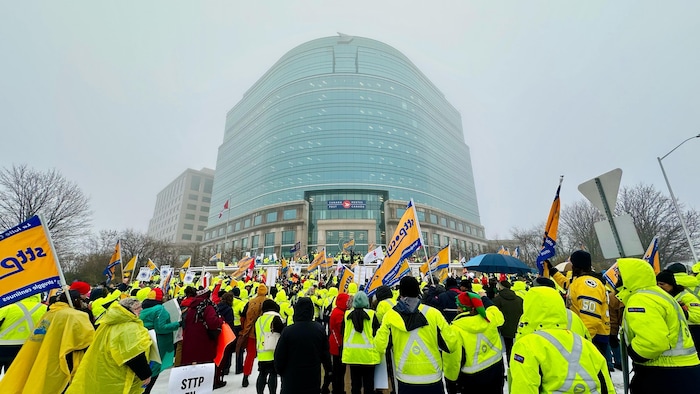 Des postiers manifestent devant un immeuble de Postes Canada.