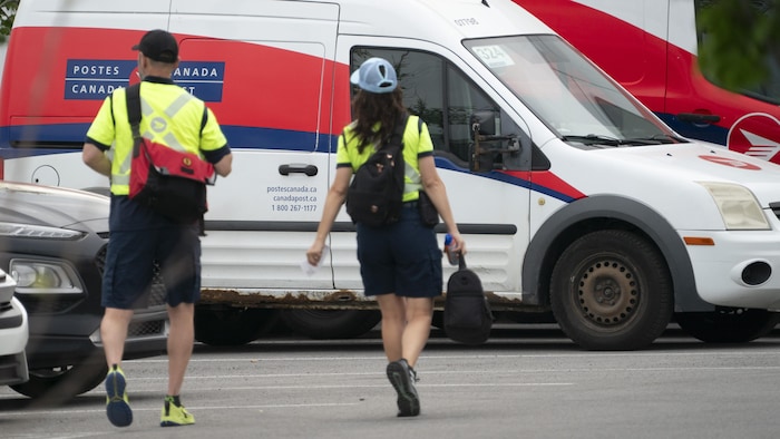 Deux employés de Postes Canada marchent dans un stationnement de la société d’État.