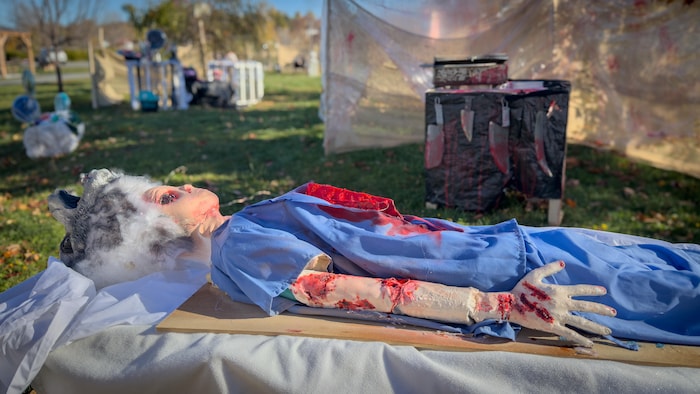 Mannequin ensanglanté en blouse médicale installé sur une table extérieure pour le décor d'Halloween à Matane.