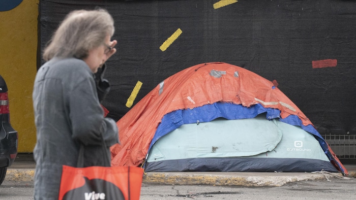Une dame passe devant une tente installée sur un trottoir à Montréal.