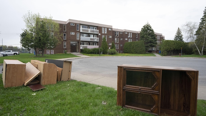 Un immeuble d'habitation au bout d'une rue en croissant. On voit des meubles à l'avant-plan, au bord du chemin.