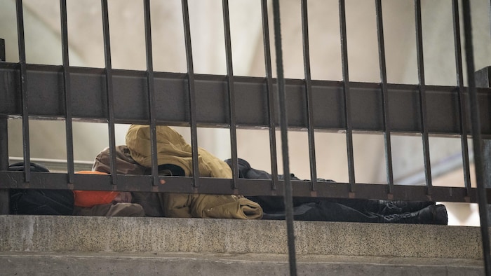 Un itinérant couché sur le sol près d'une clôture de métal dans une station de métro de Montréal.
