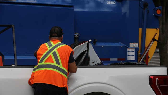 Un employé municipal jette des objets dans une boîte de camionnette.