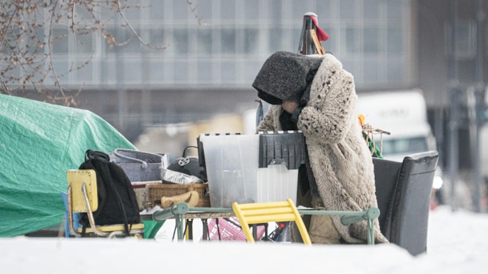 Une personne itinérante penchée sur ses biens, à côté d'une bâche, en hiver.