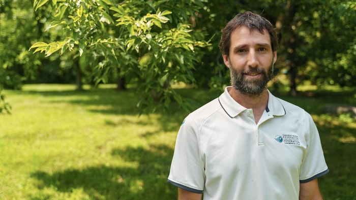 Un homme avec une petite barbe et un polo blanc debout dehors.