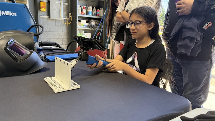 Une jeune fille tient un outil technique, dans un atelier de soudure.
