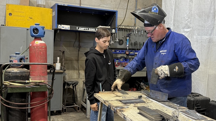 Un homme avec un casque de soudure sur la tête montre quelque chose à un enfant.