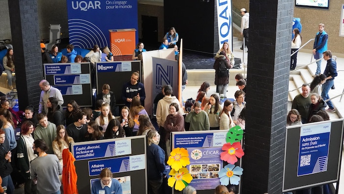 Dans un hall, plusieurs kiosques de l'UQAR sont consultés par une foule de visiteurs.