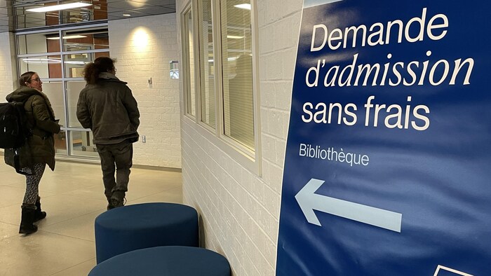 Un panneau porte la mention « demande d'admission sans frais » ainsi qu'une flèche qui pointe vers une porte où deux personnes se rendent.